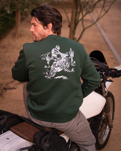 Model wearing Bike Shed Moto Desert Race Embroidered sweatshirt with a motorcycle in a dusty area