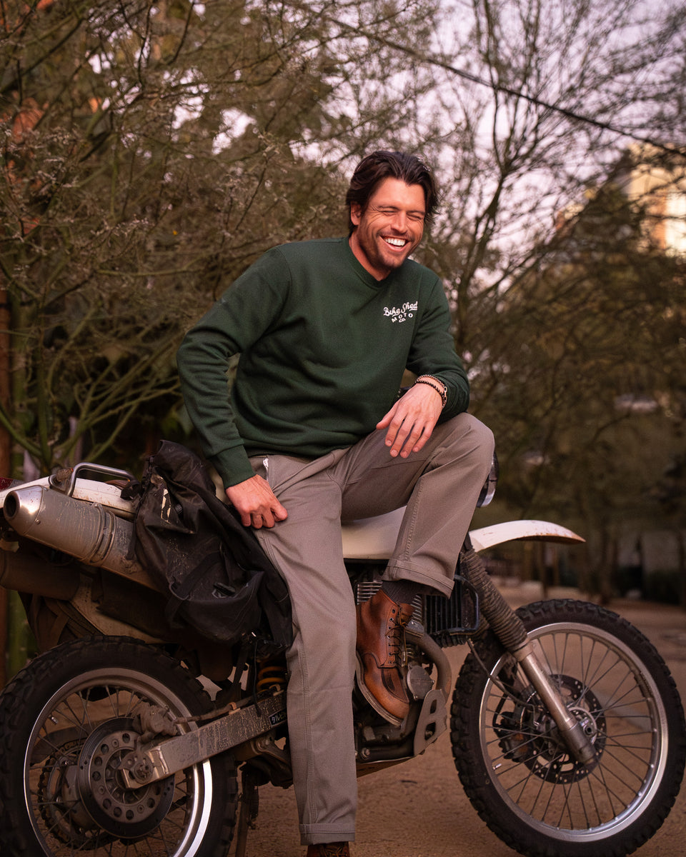 Model wearing Bike Shed Moto Desert Race Embroidered sweatshirt with a motorcycle in a dusty area