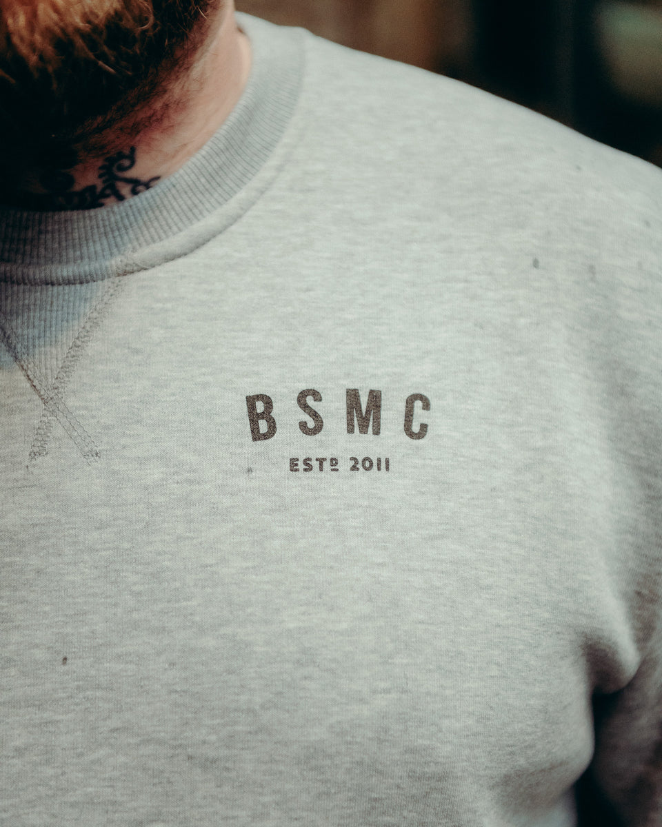 Model wearing Grey Bike Shed Moto Co ESTD Logo Sweatshirt on brick driveway