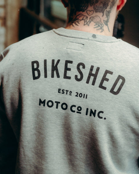 Model wearing Grey Bike Shed Moto Co ESTD Logo Sweatshirt on brick driveway