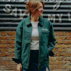 Model wearing green motorcycle jacket in front of a brick wall with graffiti.