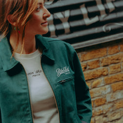 Model wearing green motorcycle jacket in front of a brick wall with graffiti.