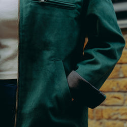 Model wearing green motorcycle jacket in front of a brick wall with graffiti.