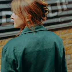 Model wearing green motorcycle jacket in front of a brick wall with graffiti.
