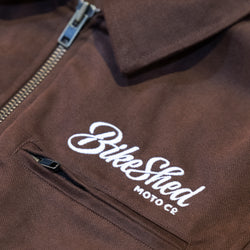 Brown twill motorcycle jacket with 'Bike Shed Moto Co' logo on a close-up of the chest area.