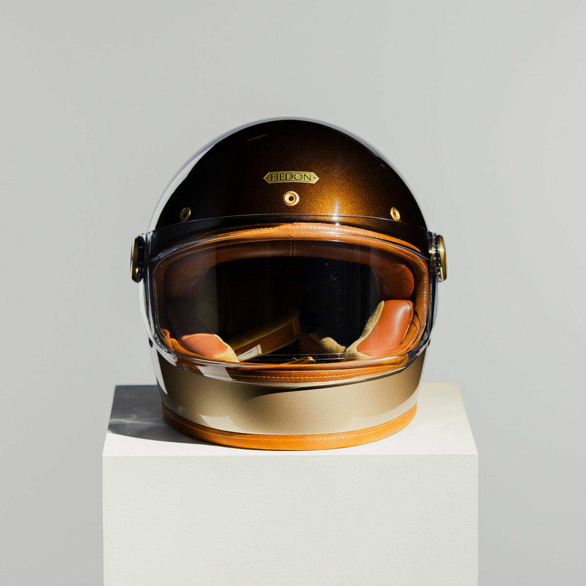 Helmet with a reflective visor on a white pedestal against a light gray background