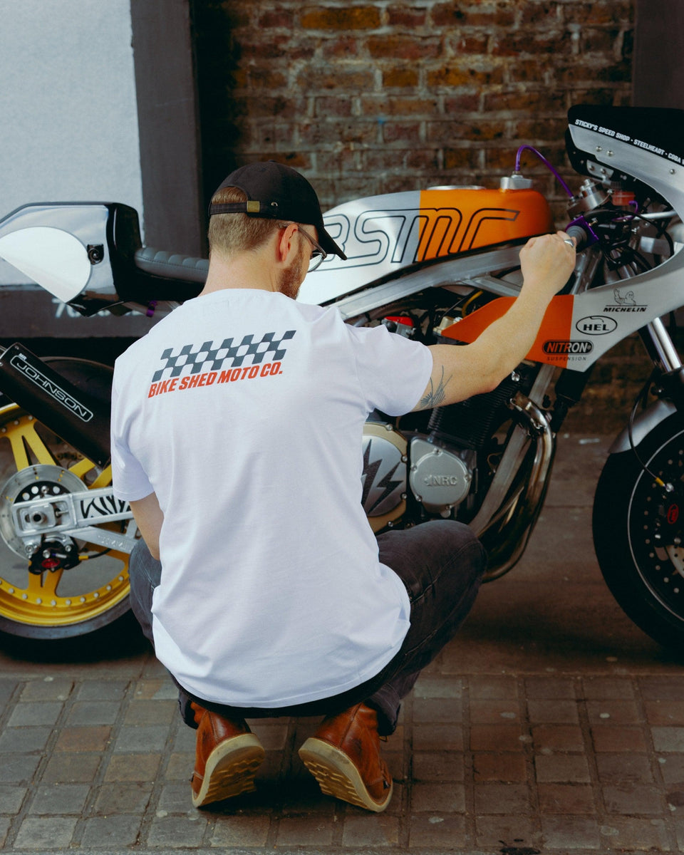 Model wearing Bike Shed Motorcycle Race T-Shirt White next to a custom motorcycle.